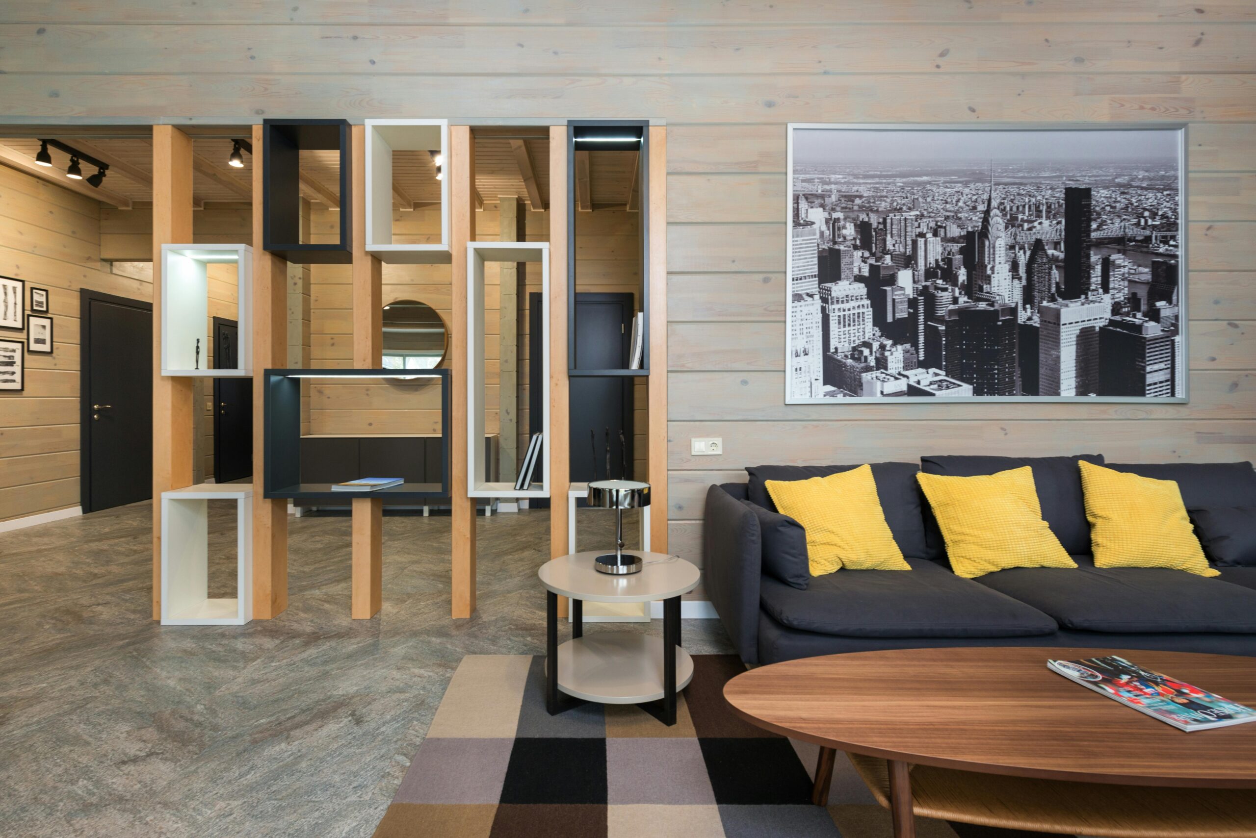 Modern apartment with sofa placed near round table with stylish geometric shelves separating living room from corridor